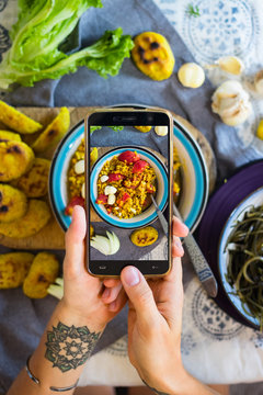 Woman hands takes photography of food on table with phone. Dinner, lunch. Indian curry lentil with tomatoes. Smartphone photo for social networks or blogging post. Vegetarian, healthy, organic