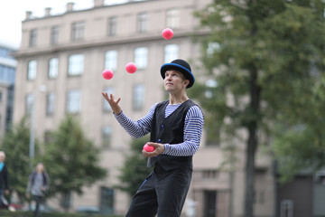 A male clown juggles with red balls in the town square