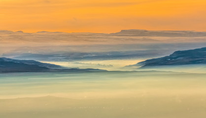 Mountains in the fog, haze. The Main Caucasian Range. Multicolored background. Mountains at sunset. Winter fog.