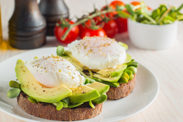 Avocado toast, cherry tomato and poached eggs on wooden background. Breakfast with vegetarian food, healthy diet concept.