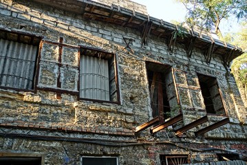 Fototapeta premium The facade of the old destroyed house is gray brown with boarded up windows