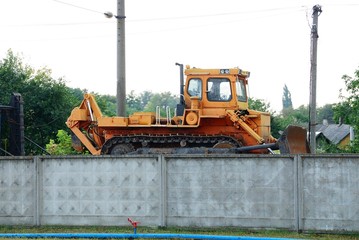 one large orange tractor stands at the concrete fence