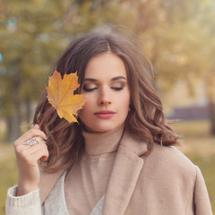 Autumn woman outdoor portrait. Perfect female model with healthy hair long bob haircut, makeup and fall leaves in hand walking in autumn park