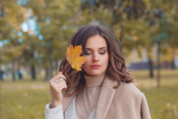 Fashion beauty portrait of perfect woman in fall park outdoors. Autumn female model brunette with wavy hair and makeup