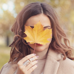 Beautiful autumn woman holding yellow maple leaf outdoors. Romantic girl in fall park