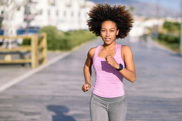 Black woman, afro hairstyle, running outdoors in urban road. - Powered by Adobe