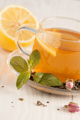 Closeup of cup of tea with tea leaves, mint on vintage wooden background. Black herbal tea with lemon, ginger and honey. hot winter drink