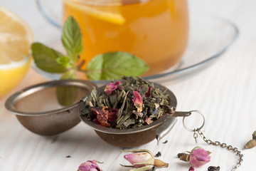 Closeup of cup of tea with tea leaves, mint on vintage wooden background. Black herbal tea with lemon, ginger and honey. hot winter drink