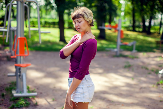 Young woman feeling pain in her shoulder, neck during sport workout in the park. Sport, medicine and people concept
