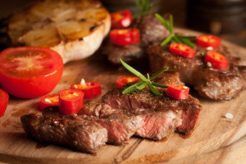 grilled fillet steak with tomatoes and roast vegetables on an old wooden board, background.