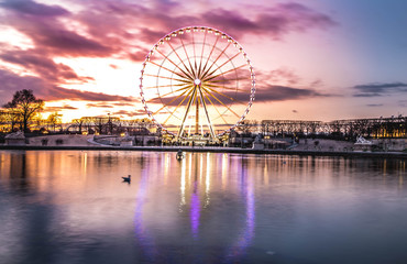 Illuminated ferris wheel with colorful sunset.