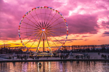Illuminated ferris wheel with colorful sunset.