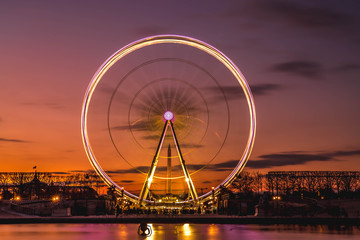Illuminated ferris wheel with colorful sunset.