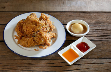 Fried chicken in white dish with souce and mash potato on wooden table.