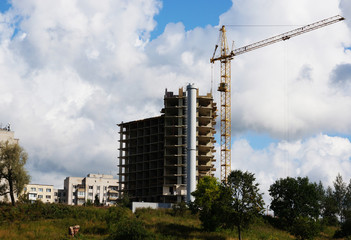 The basis of a house under construction, a working tower crane against the blue sky in summer weather.