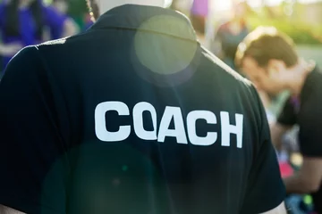 Gordijnen Sport coach in black shirt with white Coach text on the back standing outdoor at a school field, with morning lens flare © kudosstudio