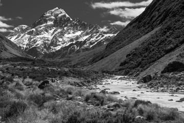 Mount Cook/Aoraki from the Hooker River valley with two hikers resting on a large rock. Black and white.