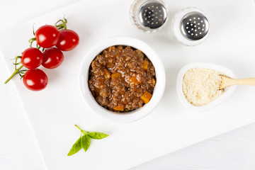 Sauce Bolognese, Parmesan cheese, a branch of tomatoes. Basil and spices. In a white plate. The background is white. Italian food. Copy space. Top view. Horizontal shot.