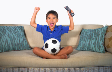 young hispanic boy happy and excited watching football game on television at home living room couch celebrating scoring goal gesturing cheerful as kid soccer crazy fan