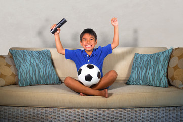 young hispanic boy happy and excited watching football game on television at home living room couch celebrating scoring goal gesturing cheerful as kid soccer crazy fan