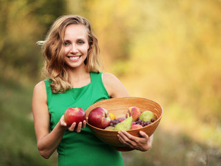 Kobieta w zielonej sukience trzymająca miskę z owocami