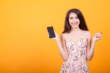 Naklejka premium Cute young woman pointing on her phone in studio on yellow background.