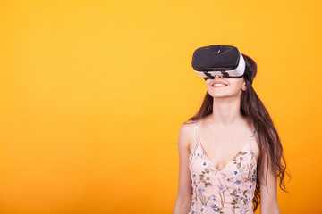 Attractive woman wearing virtual reality glasses. VR headse in studio over yellow background