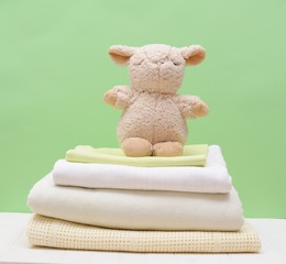 Stack light blankets and decorative toy lamb on a greeen background isolation.