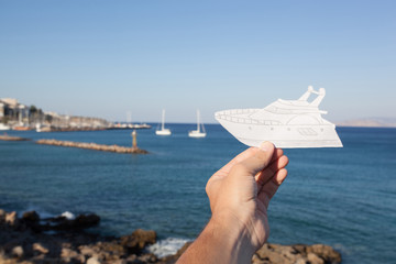 Dream to have a yacht. Hand holding a paper boat on the sea