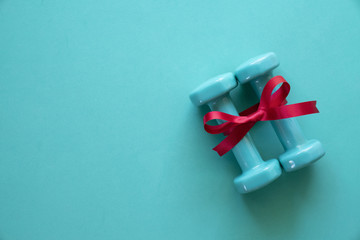 two green dumbbell with red gift bow on a green table background, sport and healthy concept