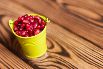 Full metal green bucket of red ripe fresh seeds of pomegranate on old brown weathered rustic planks