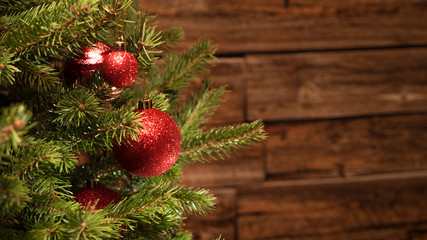 Detail of a christmas tree with glittering red glitter balls in front of a brown vintage wooden wall, detail shot with selective focus and copy space, no people