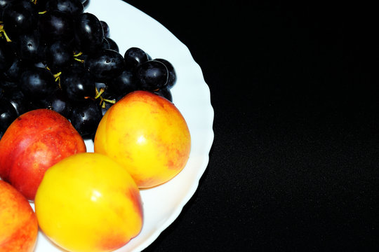 Still life of fresh fruit grapes, apples, apricots and pears on a white plate. Decorative wooden background. Ripe juicy sweet fruits. Vegetarian diet food.