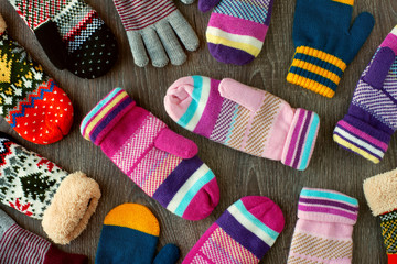Mittens for winter. View from above. Many multicolored mittens on a wooden background. Warm clothing for hands in the cold season.