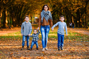 Young happy mother with her three smiling sons wearing denims and walking in the autumn park. Mom with her children on the autumn background.