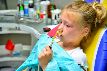 A little girl is curing a tooth at a dentist at a reception sitting on an armchair in the doctor's office.