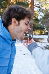 Girlfriend feeding a pineapple from a tree to her boyfriend joking in the snow a sunny day 
