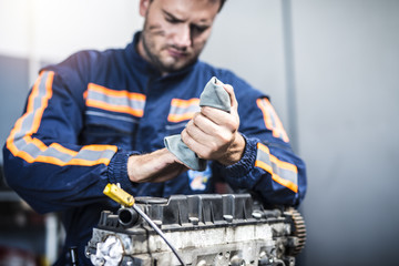 Serious professional mechanic wiping hands with rag after hardworking on car engine. Service and maintenance.  