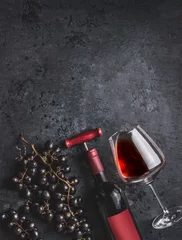 Papier Peint photo Vin Red wine bottle with vintage corkscrew, glass and grapes on retro black background, top view.