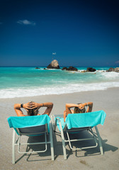 Fototapeta na wymiar Couple on sunbeds relaxing at the beach in Lefkada
