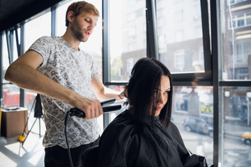 Obraz premium Beautiful woman happy while hairdresser is straightening her hair in salon. New haircut or hairstyle for young woman.
