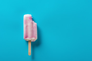 strawberry flavor popsicle with a bite on a blue background