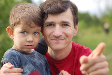 Son and dad rest together in the nature at sunset, they are happy and smiling because they are well together