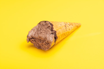 chocolate flavor ice cream cone with some bites on a yellow background