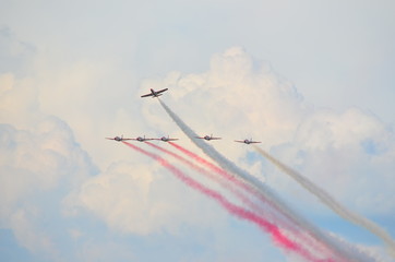 Formation of six stunt jets flying on cloudy sky leaving red and white smoke trails