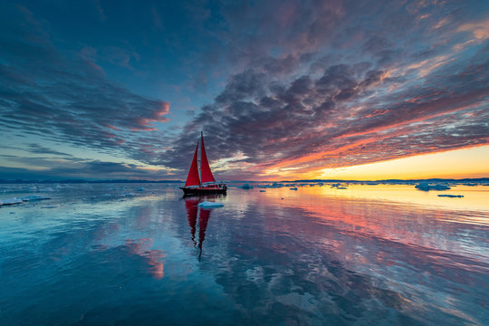 Greenland midnight Sunrise mirror panorama with red sail ship	