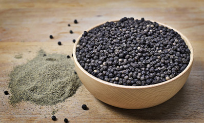 Black peppercorns and milled pepper, arrangement in a wooden bowl. Close up shot of black pepper, cooking ingredient scene and wooden table. Top view.