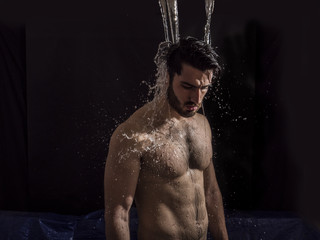 Shirtless handsome young man with water splashes on his face and chest in studio shot