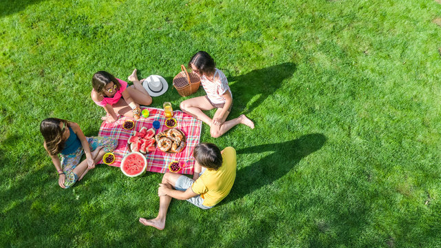 Happy Family Having Picnic In Park, Parents With Kids Sitting On Grass And Eating Healthy Meals Outdoors, Aerial Drone View From Above, Family Vacation And Weekend Concept
