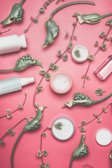 Fototapeta na wymiar Beauty flat lay with various facial cosmetic products with mock up, leaves and green flowers on pastel pink desktop background. Modern skin care layout, top view